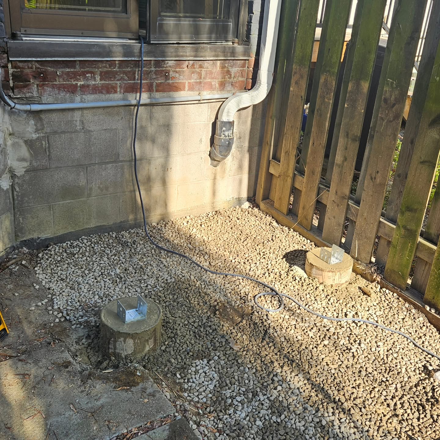 New concrete footings with post brackets set into fresh gravel after the old structure was removed