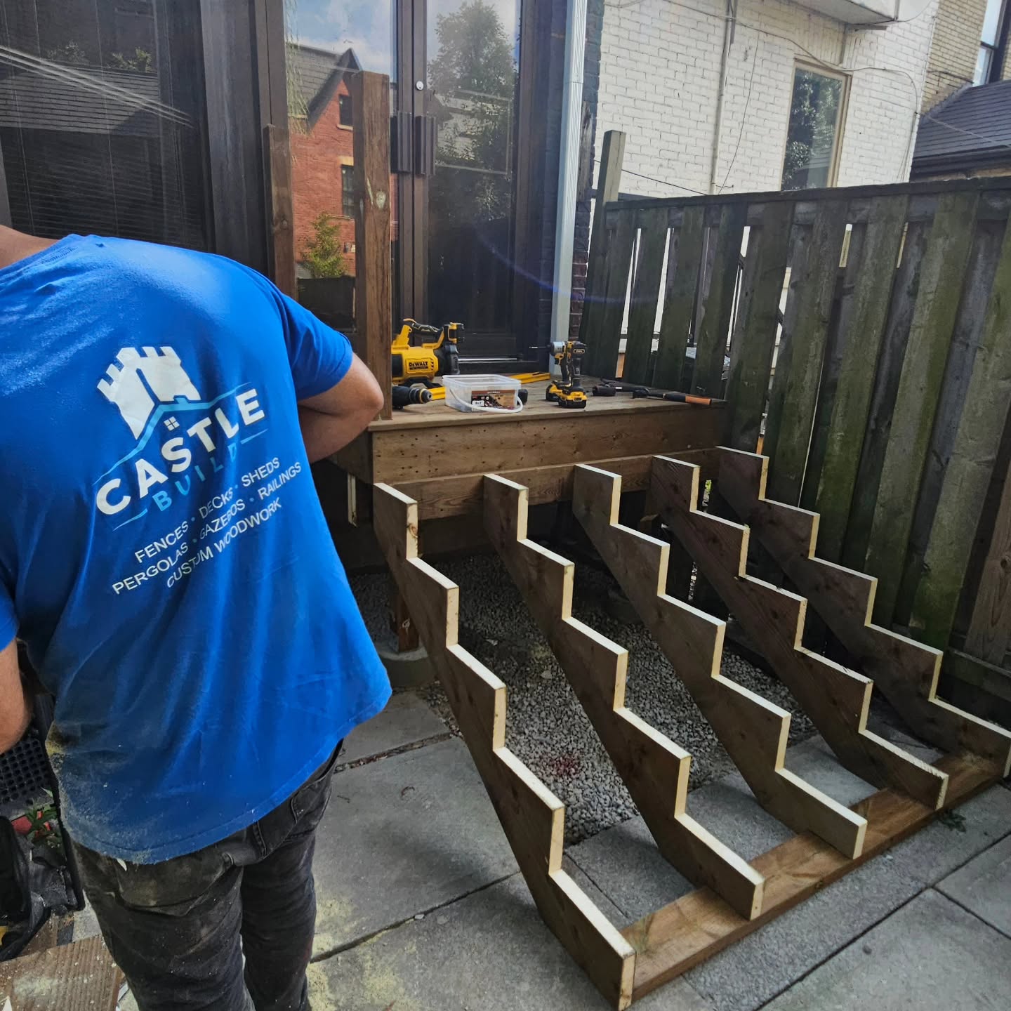 A Castle Build carpenter in a branded shirt working on the cut stair stringers beside the new deck